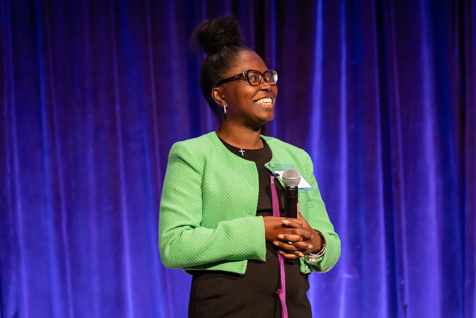 Smiling, young Black woman holding a microphone on stage