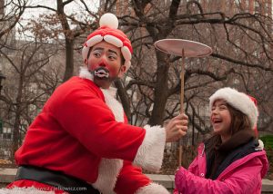 Asian man in a Santa costume helping a girl spin a plate on a stick