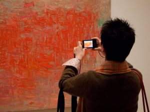 A woman photographing a painting in a museum