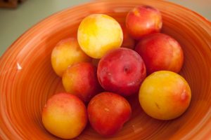 A bowl of plums in an orange earthenware bowl