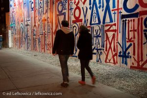A couple strolls past a wall of graffiti on Houston Street