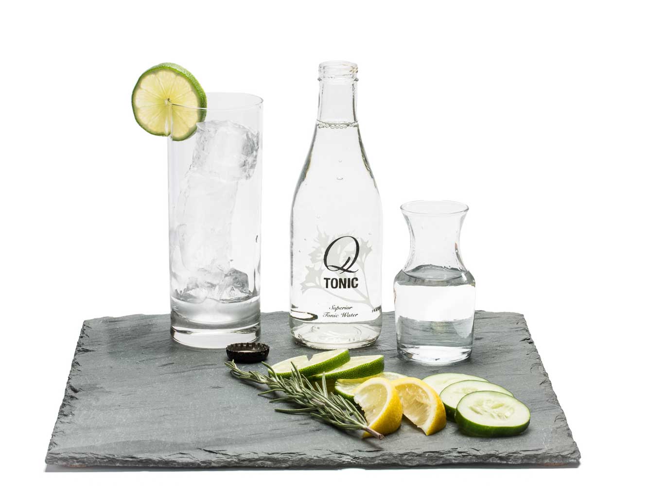 Glass with ice and lime, bottle of tonic, beaker of gin on a slate