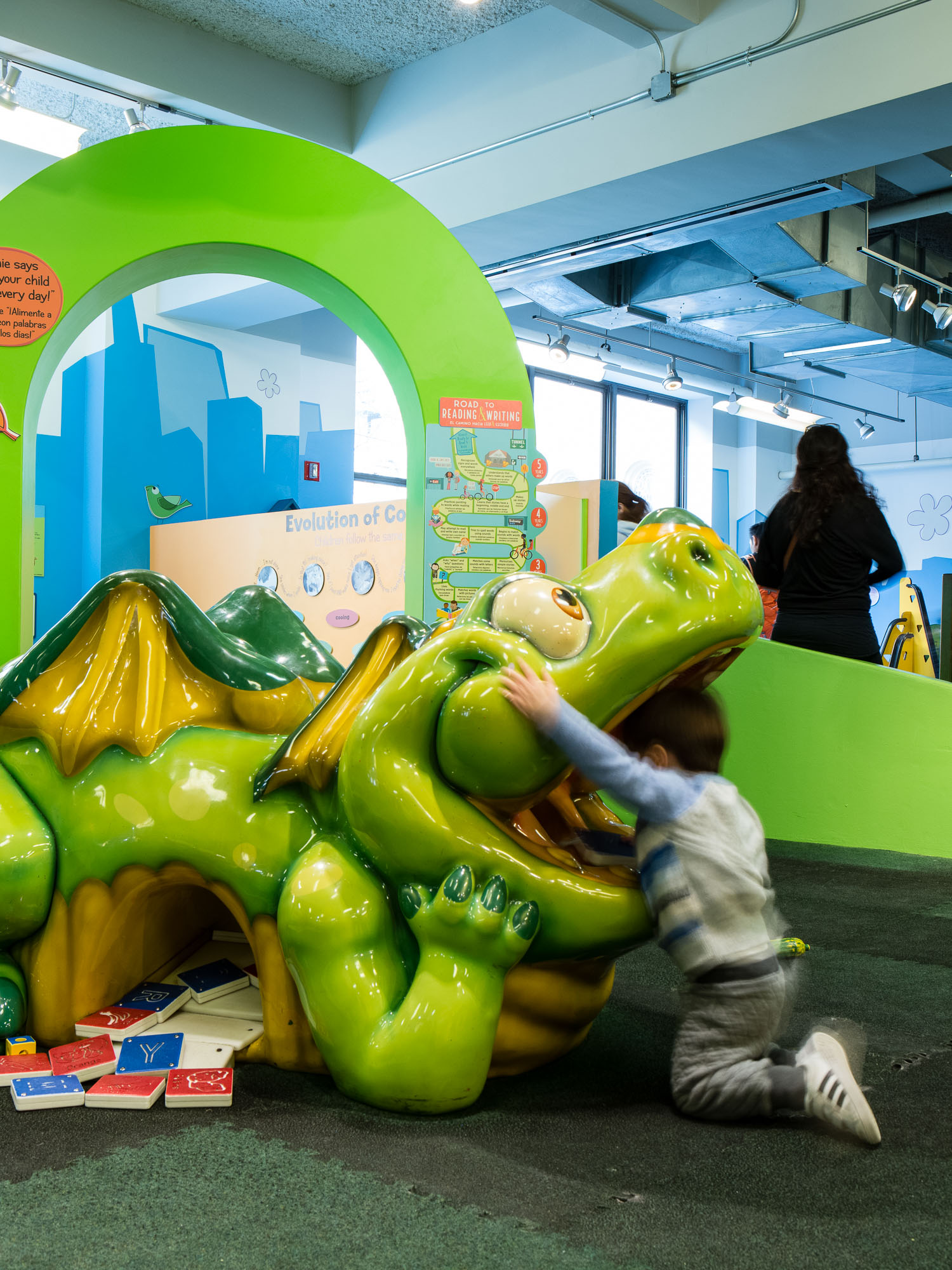 A child with his head in the jaw of a giant green dragon in a place space in the Children's Museum of Manhattan.