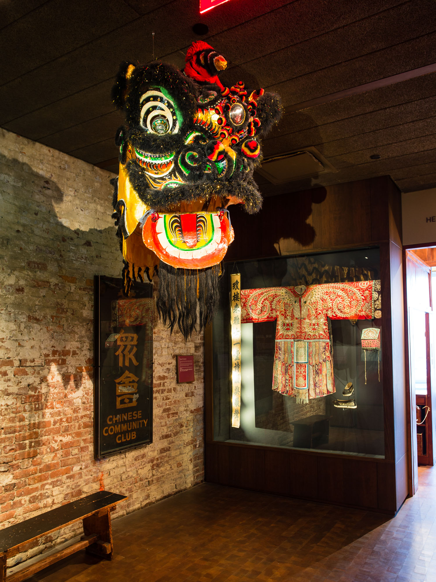 A dragon mask hangs from the ceiling, and a Chinese opera costume in a glass case in the Museum of Chinese in America