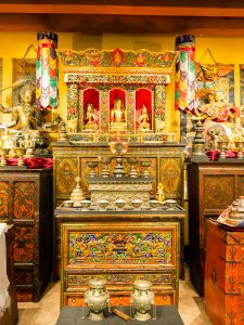 A nineteenth-century shrine cabinet (chosham) is at the center of the shrine room at the Rubin Museum, with a Tibetan offering table in the foreground.