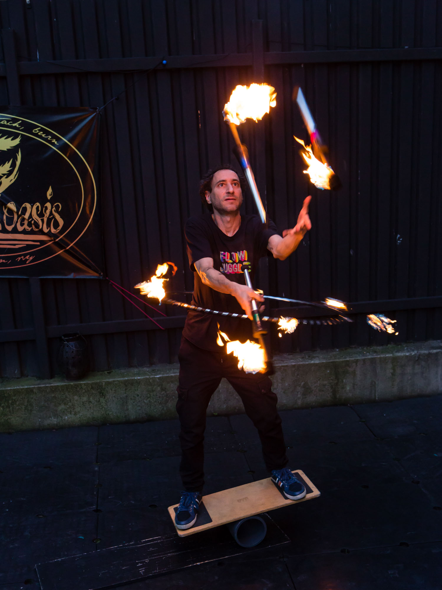 Martin Kuborn juggling flaming torches while twirling a hula-hoop with six flaming torches around its perimeter, all while balanced on a balance board at The Floasis.