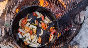 Vegetables cooking in a cast iron dutch oven over an open fire at an autumn beach picnic