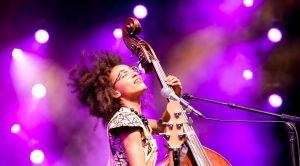 Esperanza Spalding in concert playing an upright bass with bright stage lighting behind her