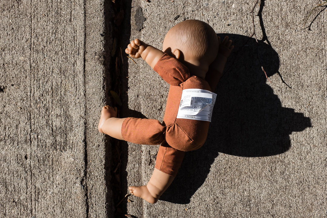 A baby doll appears to be climbing up a crack in a sidewalk