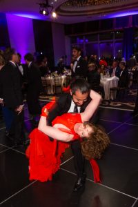 A couple dancing, the woman in a red dress being dipped, at a gala for the New York Pops