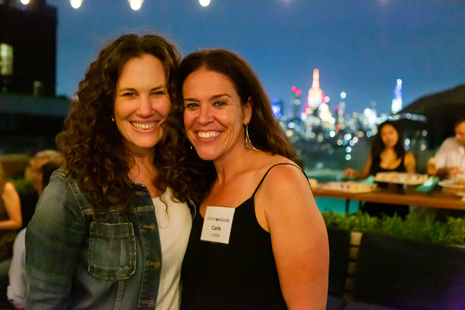 Two women on a rooftop in the evening with New York City in the background