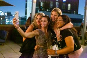 Four women on a rooftop in the evening taking a group selfie
